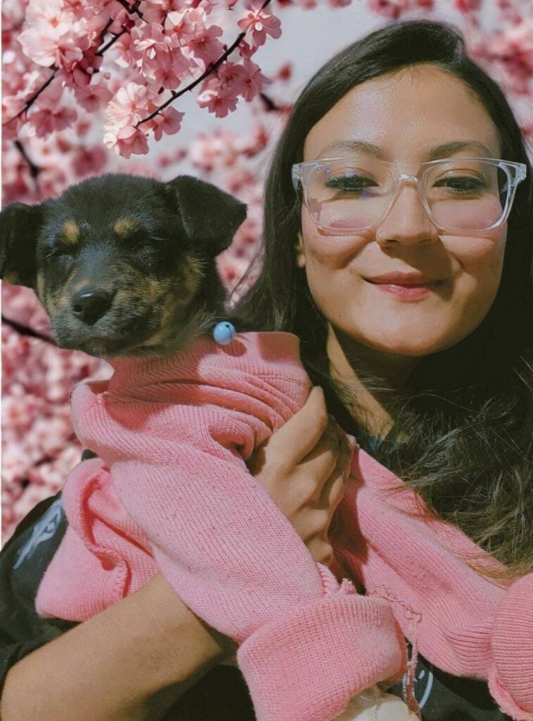 Woman smiling and holding a puppy in matching pink sweaters, set against a floral background — dogs and cats help slow cognitive decline