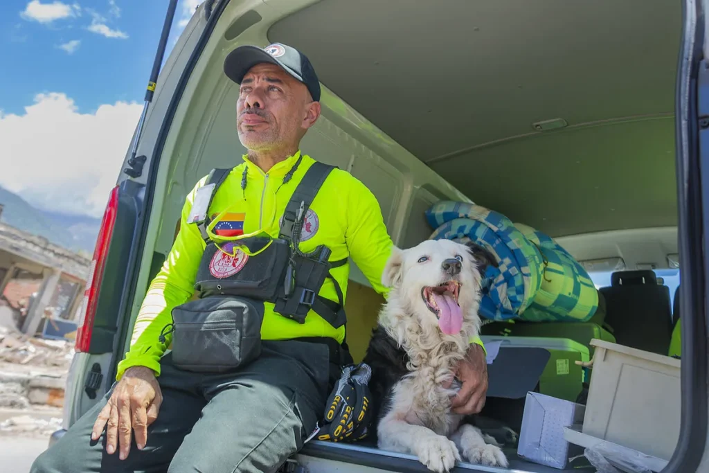 Jorge Beens sits in the open back of a rescue vehicle with Tsunami, his Border Collie search-and-rescue dog, during the earthquake response in La Guaira, Venezuela, July 2026.
