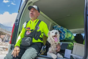 Jorge Beens sits in the open back of a rescue vehicle with Tsunami, his Border Collie search-and-rescue dog, during the earthquake response in La Guaira, Venezuela, July 2026.