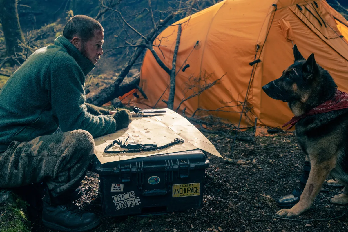 Heart of the Beast still: James Belmont reads a map beside an orange tent as Odin, a German Shepherd in a red bandana with a leg brace, sits and watches him
